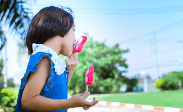 young girl eating 2 popsicles during the summer