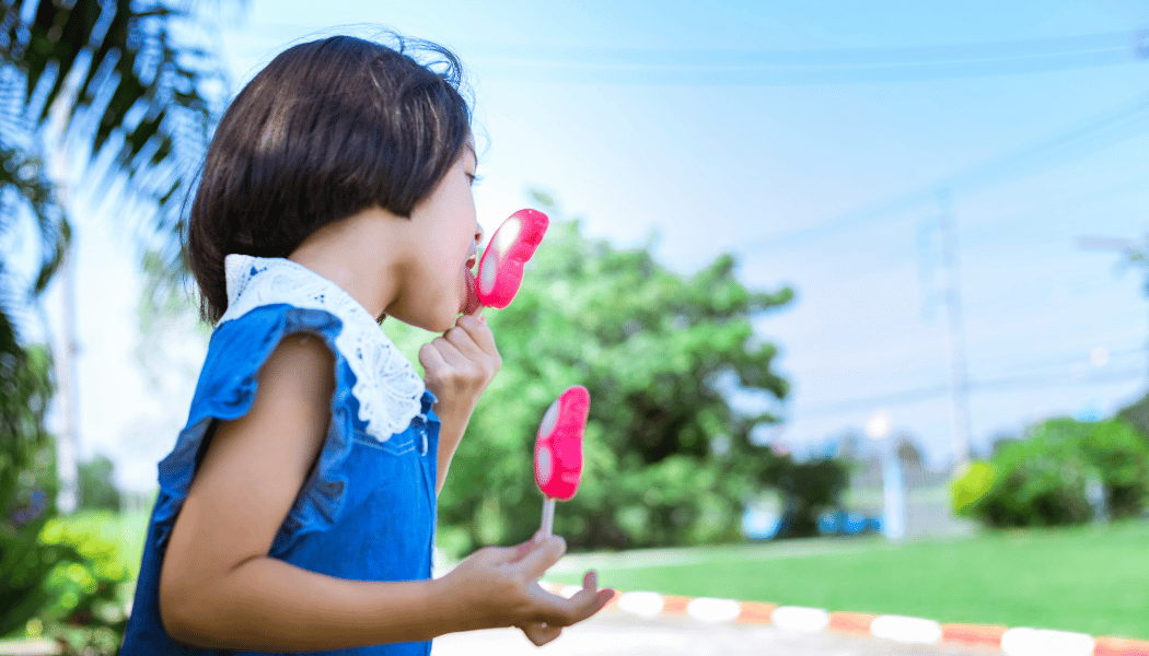 young girl eating 2 popsicles during the summer
