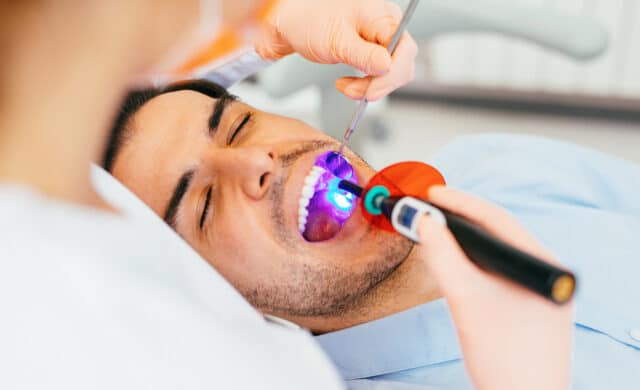 female dentist using a dental curing light after applying sealants on young man's molars