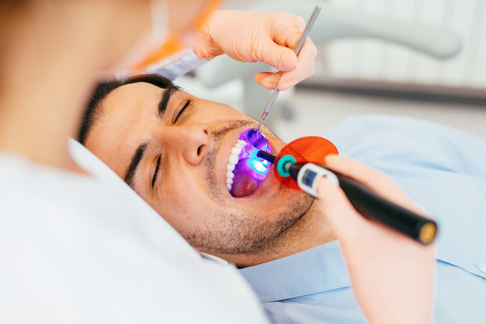 female dentist using a dental curing light after applying sealants on young man's molars