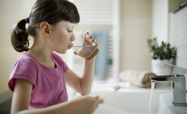 Young girl rinsing mouth in the bathroom with water after brushing teeth