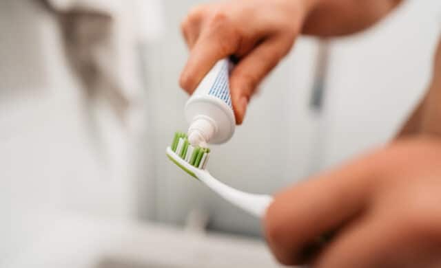 how often should you change your toothbrush blog image of adult adding toothpaste to toothbrush
